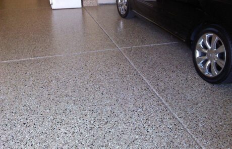 This image shows a black car in a garage that has an epoxy flake floor.