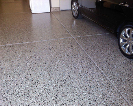 This image shows a black car in a garage. The floor has epoxy flakes on it